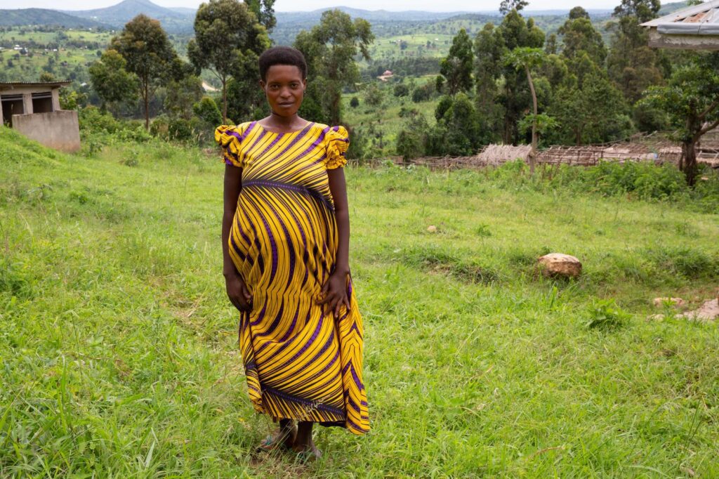 Pregnant woman in Africa standing in a green field in a yellow and maroon striped dress