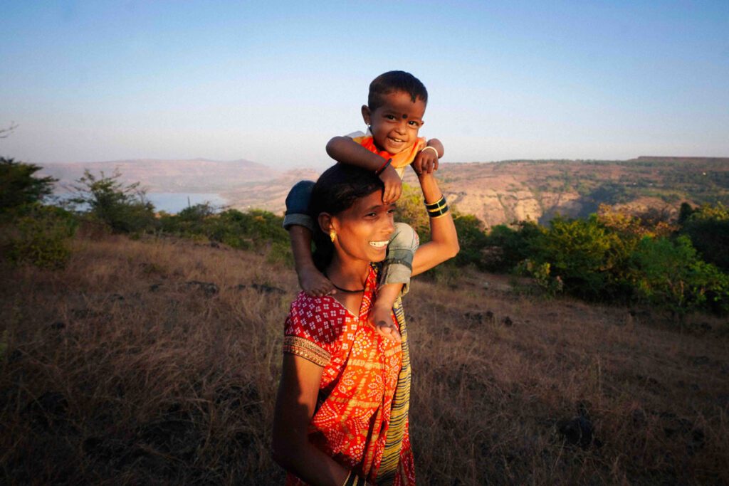 An Indian mother walks across the grass with her young son on her shoulders
