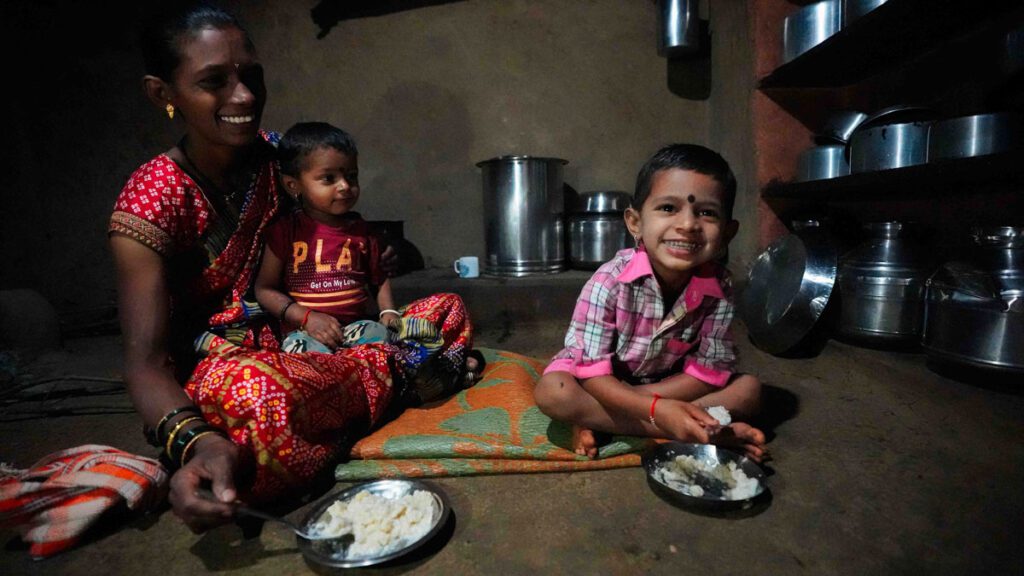 Inside their home in India, a mother sits with her two sons while they eat breakfast. 