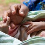 Close up of infant and midwife holding hands.