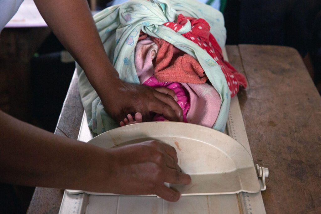 A baby is being measured by a health worker, a few toes are peaking out from the device
