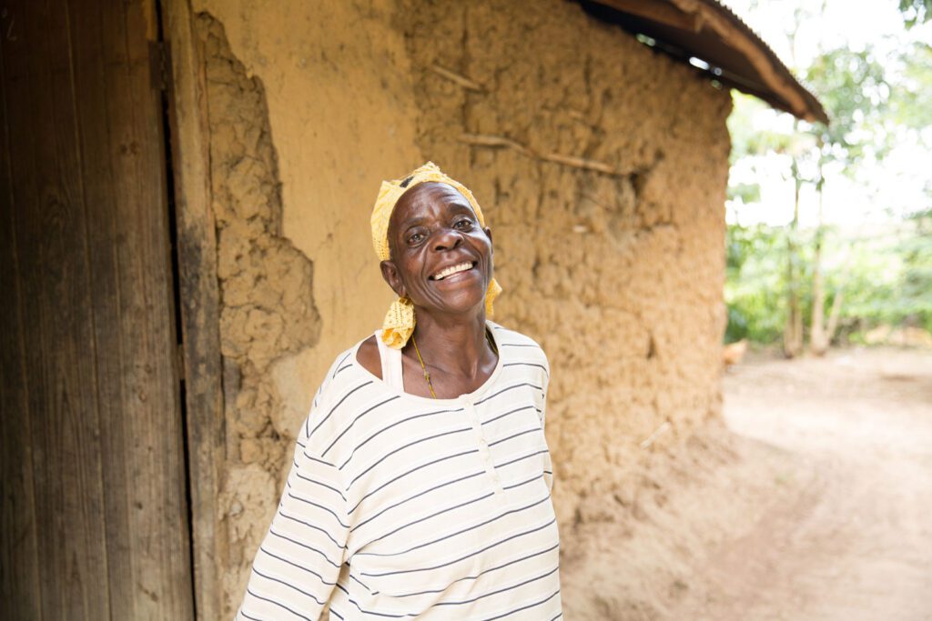 A midwife stands, smiling, in front of a home in rural Kenya