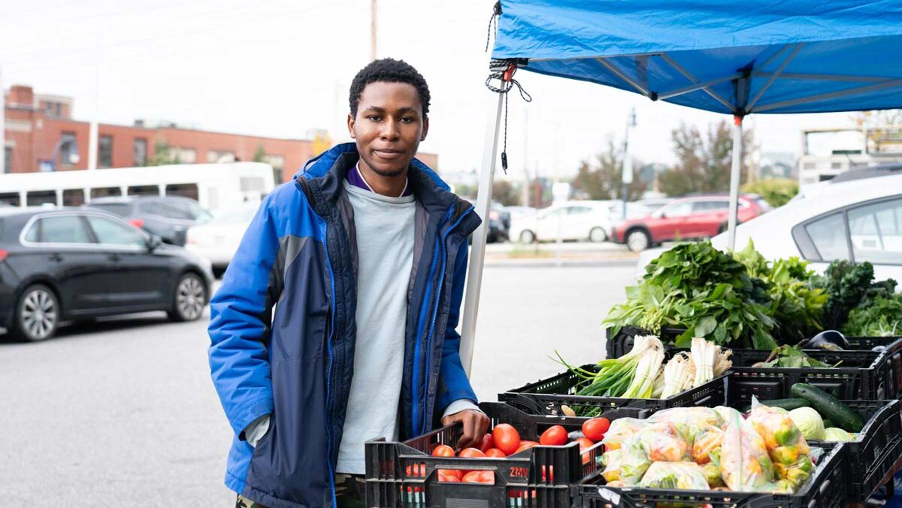 A man stands next to a vegetable stand in the TOC parking lot