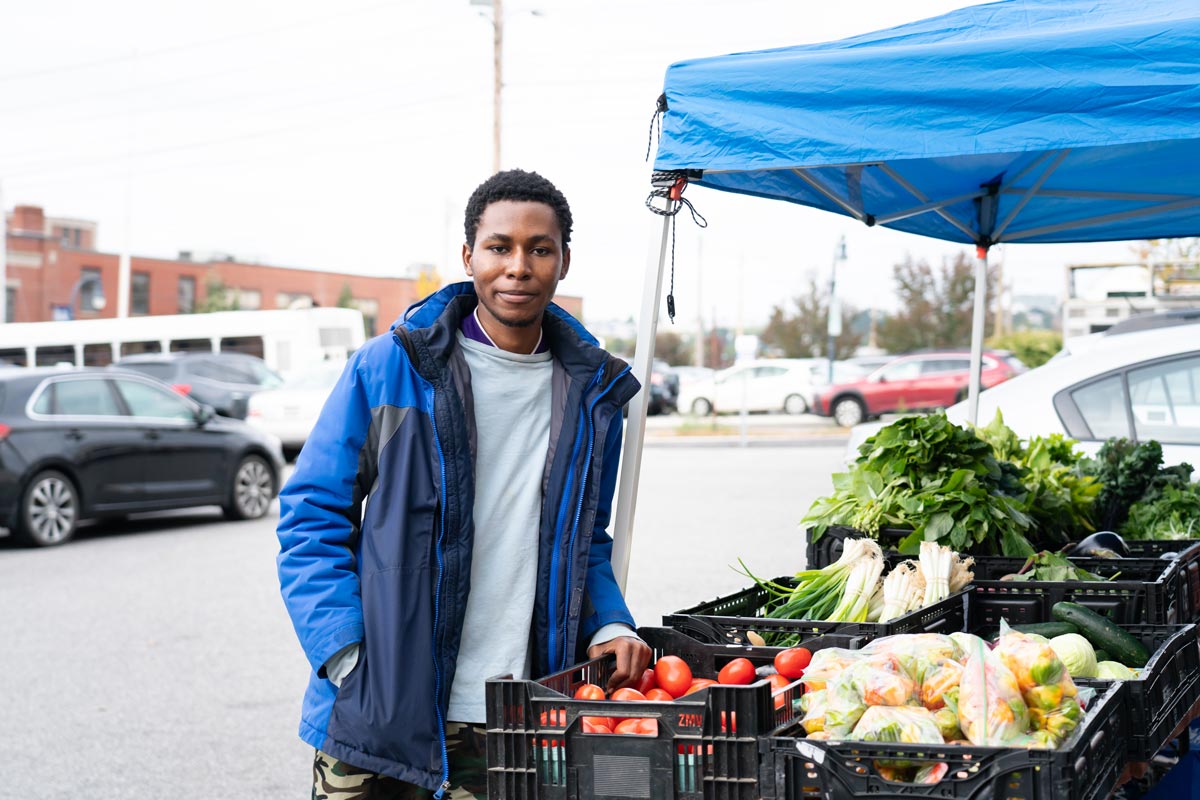 A man stands next to a vegetable stand in the TOC parking lot