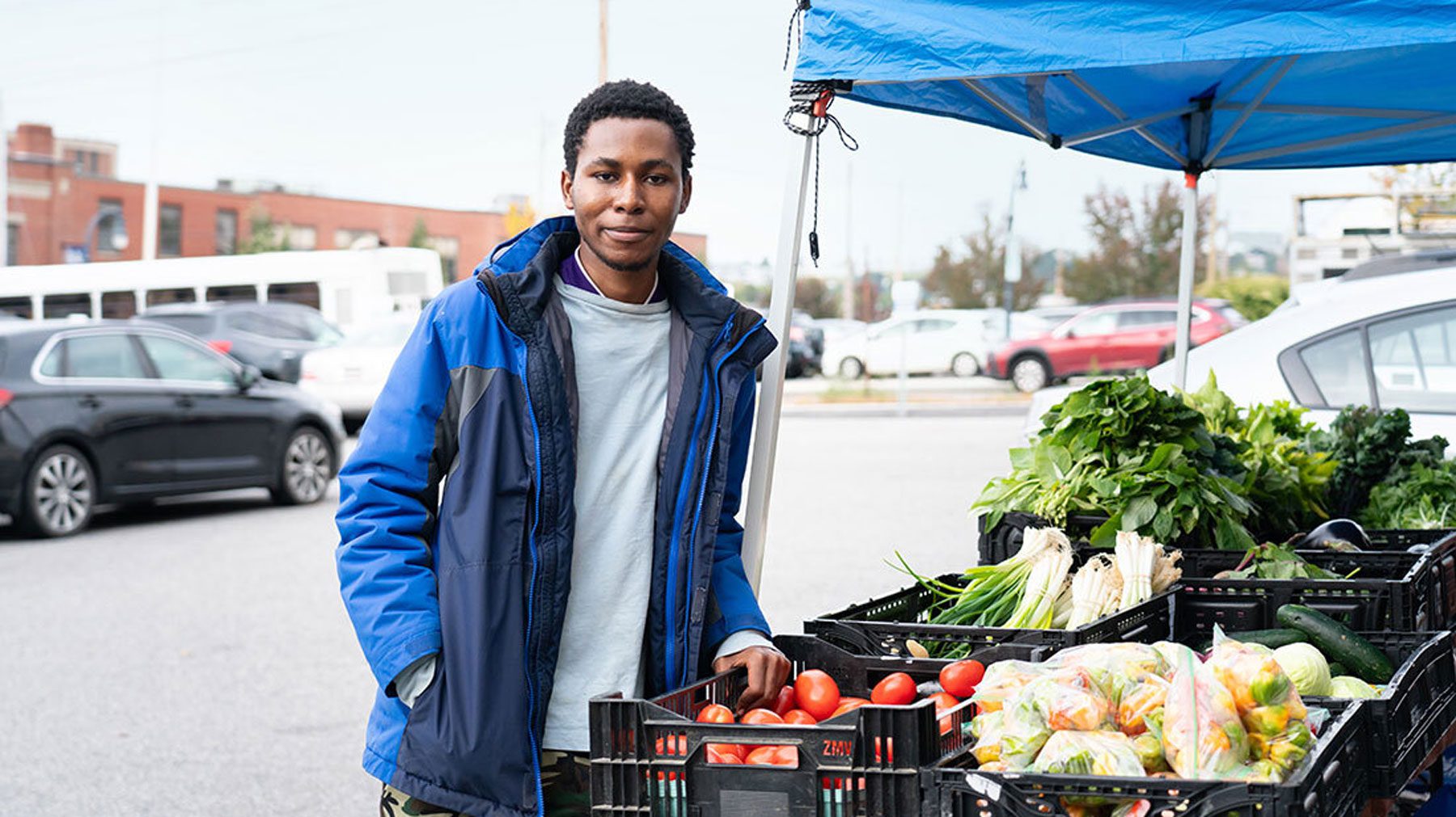 A man stands next to a vegetable stand in the TOC parking lot