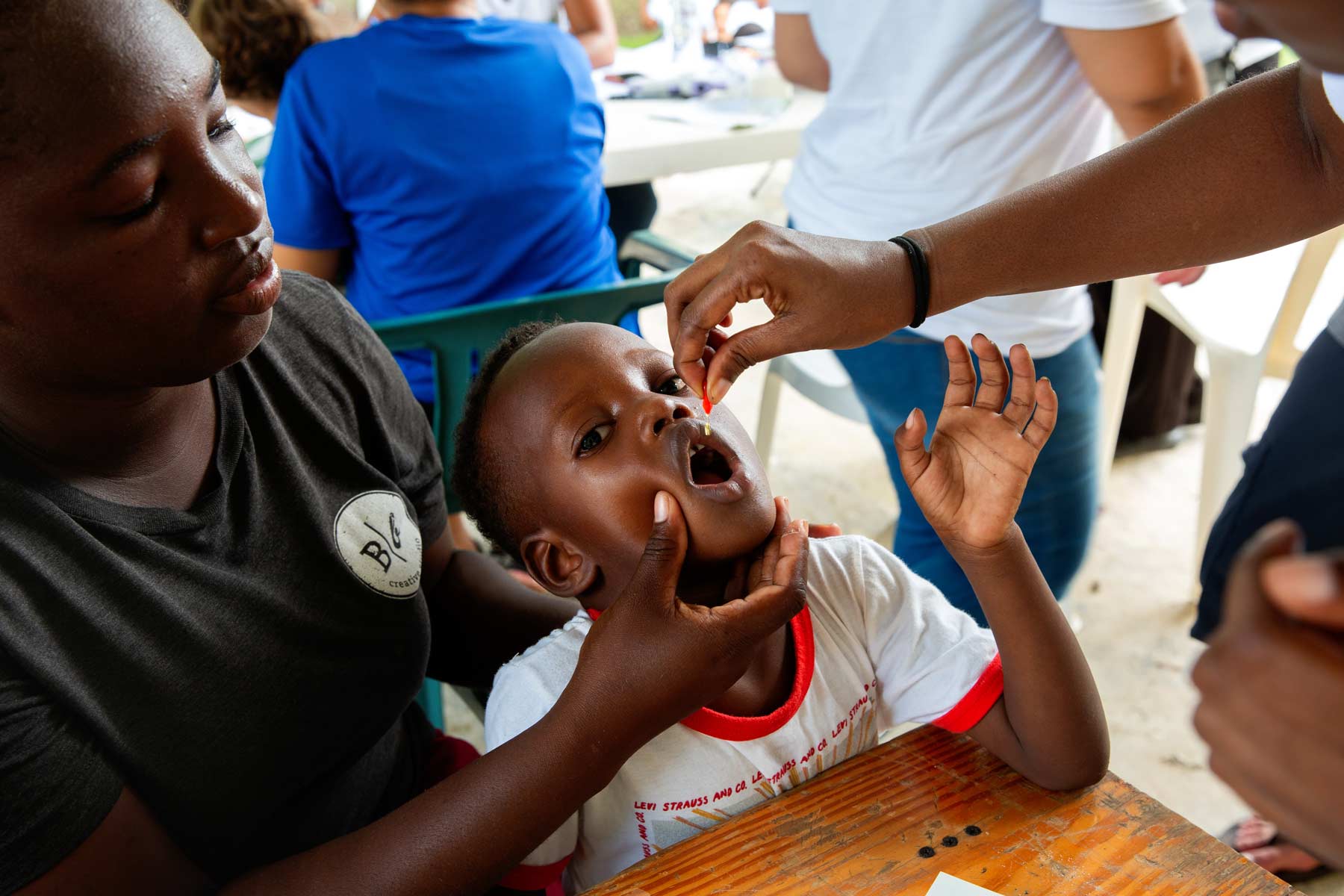 A boy receives a dose of vitamin A, assisted by his mother.