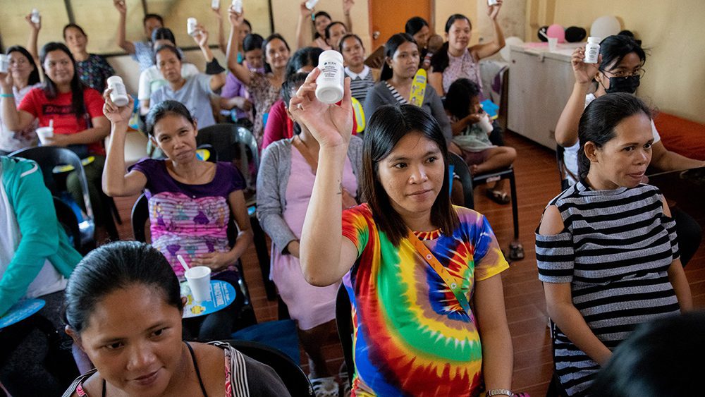 A room of women seated holding up bottles of UNIMMAP MMS.