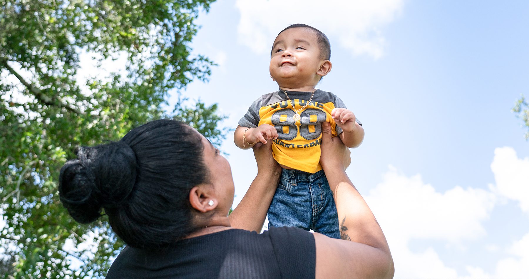 A mom holds her baby boy up to the sky as he smiles.