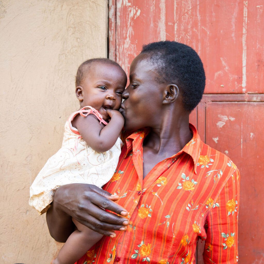 Ugandan mother holding and kissing infant child on the cheek.