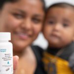 A woman holds her infant son and bottle of Vitamin Angels prenatal vitamins and minerals