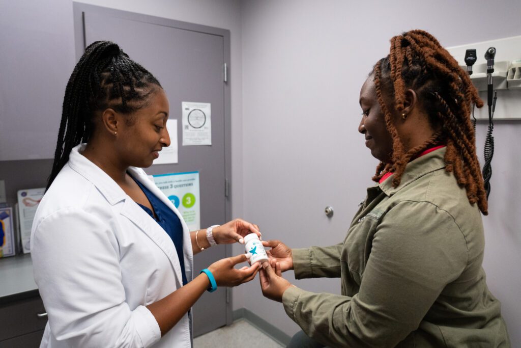Health care provider hands a bottle of prenatal multivitamins to a patient.