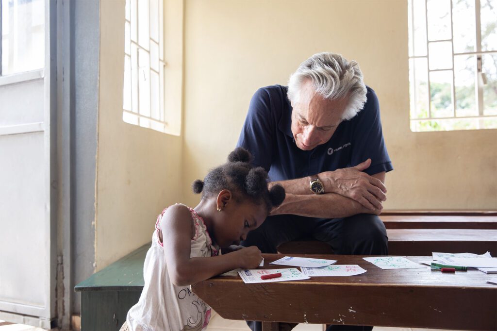 Howard watching a child write at a desk in Sierra Leone.