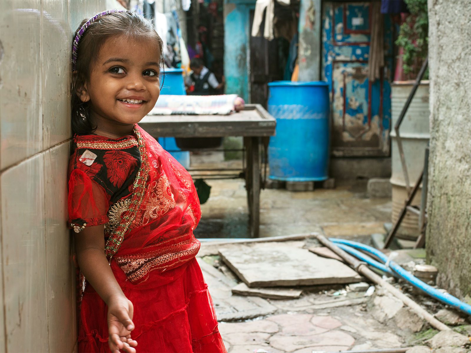 Young child smiles while leaning against a wall in India.