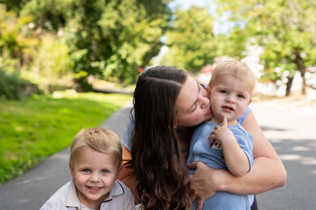 Beth kisses her son Wally on the cheek as her older son, PJ, smiles at the camera.